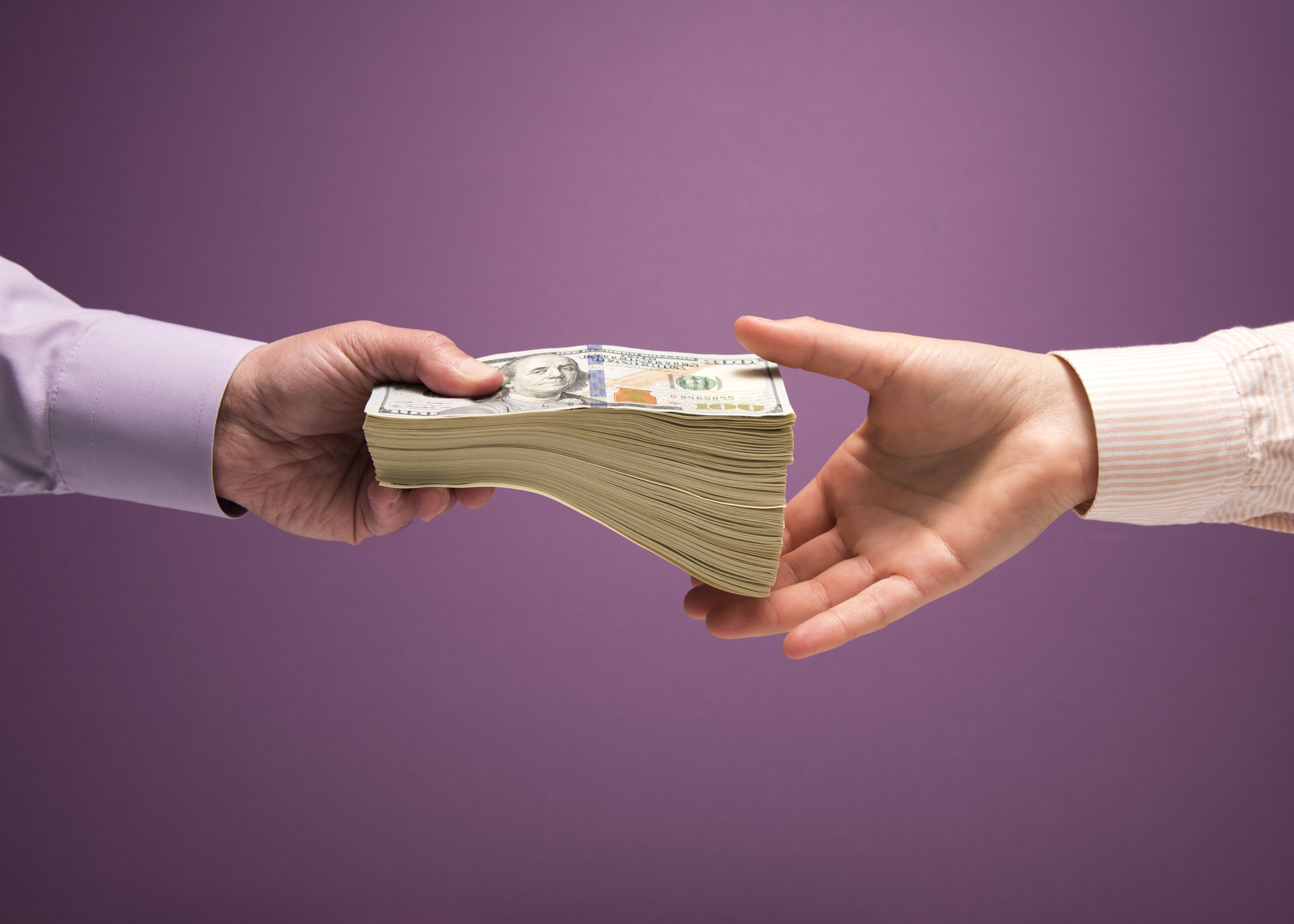 Man and woman’s hands handing pile of cash